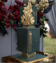 a green box with gold foil on top sitting on a table in front of flowers