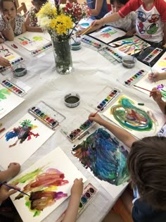 children are sitting at a table painting with watercolors and flowers in the background