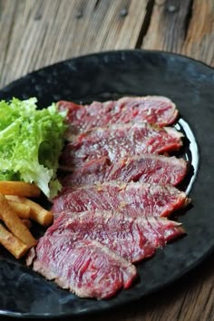 steak, fries and lettuce on a black plate sitting on a wooden table