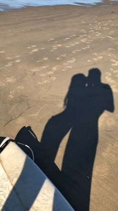 the shadow of a person holding a surfboard is cast on the sand at the beach