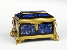 a blue and black box with gold trimmings on the top, sitting on a white surface