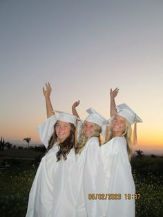 three girls in white graduation gowns and caps are posing for the camera at sunset