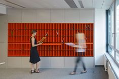 two people standing in front of a wall with orange bookshelves and red shelves