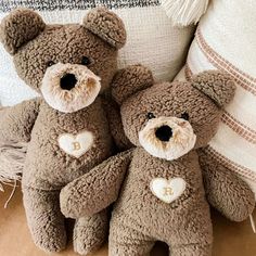 two brown teddy bears sitting next to each other on a couch with pillows behind them