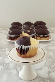 chocolate cupcakes with white frosting sitting on a cake plate next to each other