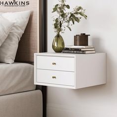 a white nightstand with two drawers next to a bed and a plant in a vase