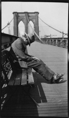 a man sitting on top of a bench next to the brooklyn bridge in black and white