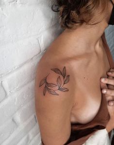 a woman with a small tattoo on her shoulder and breast is leaning against a white brick wall