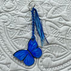 a blue butterfly keychain is sitting on a white lace tablecloth with beads and tassels