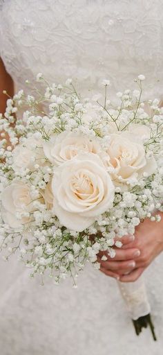 a bride holding a bouquet of white roses and baby's breath in her hands