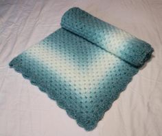 a crocheted blanket laying on top of a bed next to a white sheet