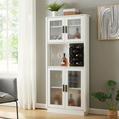 a white cabinet with wine glasses and bottles on it in a living room next to a window