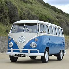 a blue and white vw bus parked on the side of a road next to a hill