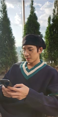 a young man sitting on a bench looking at his cell phone while wearing a hat