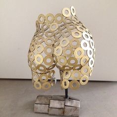 a metal sculpture with circles on it sitting on top of a block of wood next to a white wall