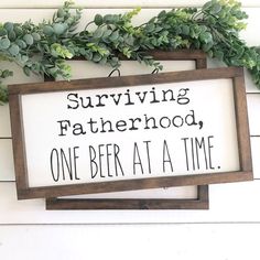 a sign that says surviving fatherhood, one beer at a time hanging on the wall