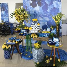 a blue and yellow dessert table with flowers on the table, plates and vases