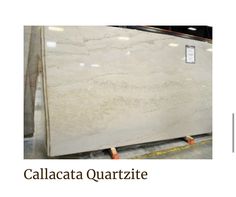 a white marble counter top sitting in a room next to a sign that says calacata quartzite