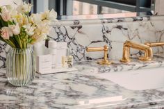 a marble counter top with gold faucets and flowers in a vase next to it