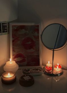 some candles are sitting on a table next to a mirror and a framed photo with lipstick prints