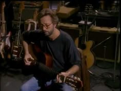 a man sitting on the ground playing a guitar in a room full of musical instruments