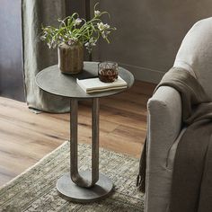 a living room with a chair, table and vase on the floor in front of a window