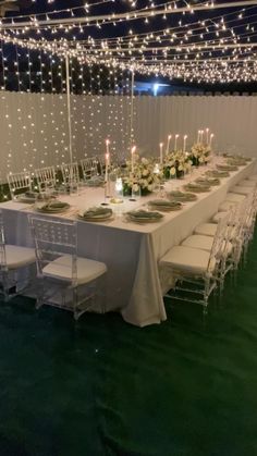 a long table is set up with white chairs and lights strung from the ceiling above it