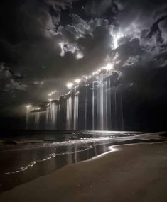 the sun is shining through clouds over the water at night on an empty beach with waves coming in