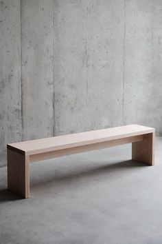 a wooden bench sitting on top of a cement floor in front of a concrete wall