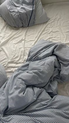 an unmade bed with blue and white striped comforter on top of it, next to pillows