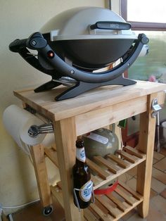 a bbq grill sitting on top of a wooden table next to a bottle of beer