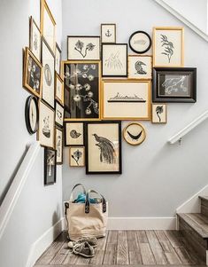 a bunch of framed pictures are hanging on the wall above a stair case with a handbag and purse