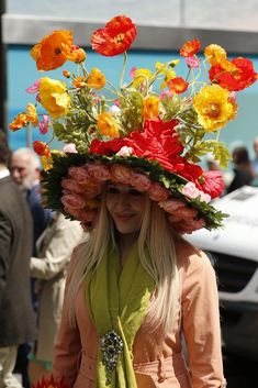 a woman wearing a large hat with flowers on it's head and scarf around her neck