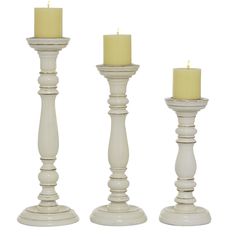 three tall white candlesticks with one candle lit