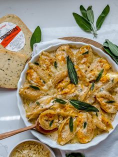 a white bowl filled with pasta and cheese on top of a wooden table next to bread