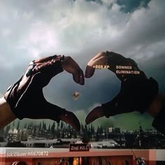 two hands making the shape of a heart on top of a television screen with buildings in the background