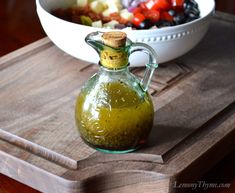 a glass bottle filled with green liquid sitting on top of a wooden cutting board next to a bowl of fruit