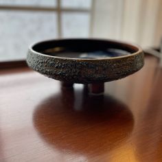 a black bowl sitting on top of a wooden table next to a window in a room