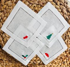 four white napkins with red and green christmas trees on them sitting in a woven basket