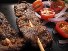 some meat and vegetables are sitting on a black plate with toothpicks in it