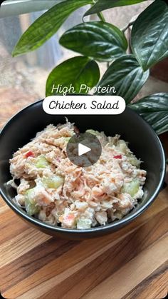 a bowl filled with chicken salad sitting on top of a wooden table next to a potted plant