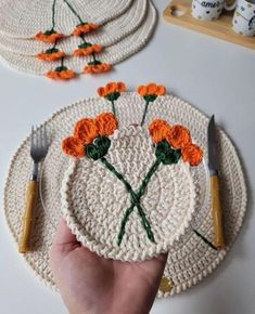 a hand is holding a crocheted plate with orange flowers on it and two forks