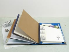 an open book on top of a table next to some papers and a boat in the background