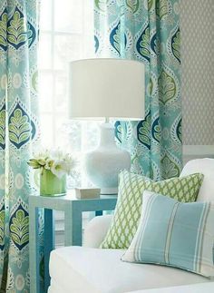 a white couch sitting next to a window covered in blue and green curtains