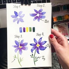 a person holding up a piece of paper with watercolors on it and flowers