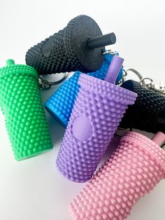 four different colored plastic objects on a white surface with keychains in the shape of cups