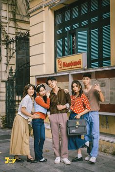 four people posing for the camera in front of a building with an advertisement on it