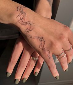 a woman's hand with tattoos and rings on her left wrist, holding onto the other