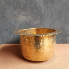 a large gold bowl sitting on top of a pink cloth covered table next to a gray wall