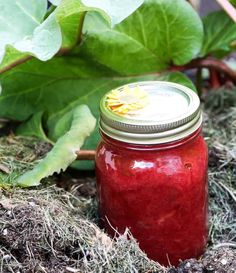 a red mason jar with a yellow flower on it sitting in the ground next to green leaves